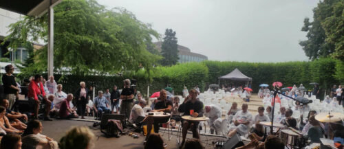 Publikum kuschelt sich um die lesenden Hans-Peter Falkner und Markus Binder von Attwenger. Da hielt das Wetter noch. Aber dann.