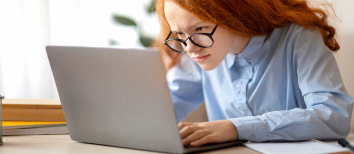Girl wearing glasses sitting at table, using laptop