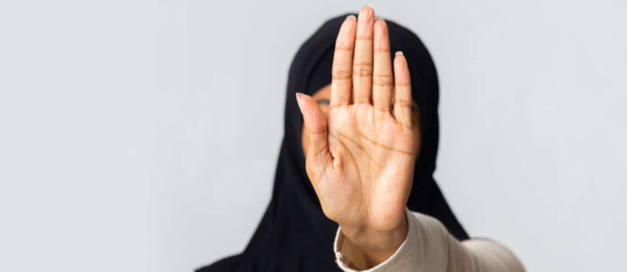 Unrecognizable muslim woman in hijab making stop gesture wit