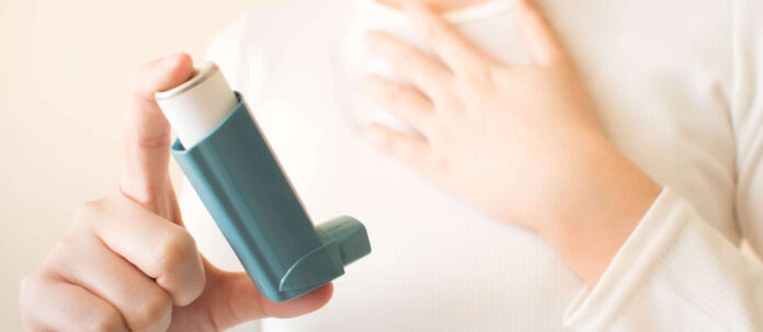 Young female in white t-shirt using blue asthma inhaler for